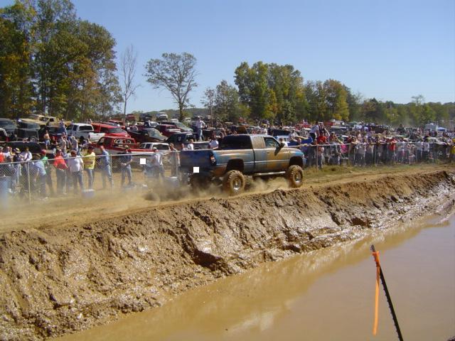 Muddy pickup truck drives through a mud pit next to a crowd of spectators