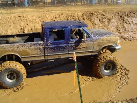 1979 Ford Bronco - Mud bogging event with a lifted blue pickup truck.