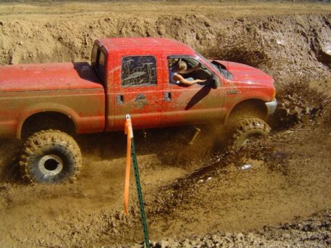 1979 Ford Bronco - A red pickup truck navigates a challenging mud pit, sending spray in all directions.