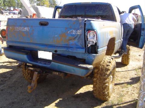 1979 Ford Bronco - Mud-covered blue Dodge pickup truck with 4x4 badging and a damaged taillight sits after an off-road event.