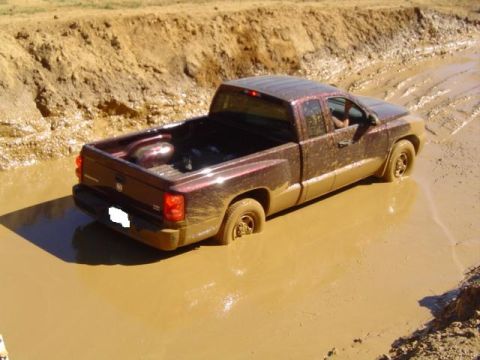 1979 Ford Bronco - A red pickup truck is stuck in a muddy track, with its tires sunk deep into the mire.