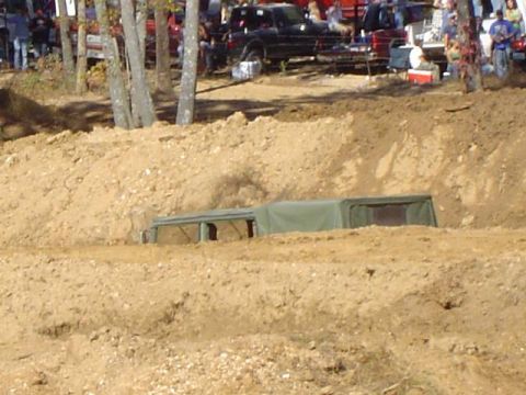 1979 Ford Bronco - A military-style vehicle is partially submerged in a muddy pit during an off-road event.