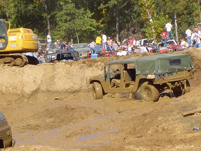 Muddy olive drab Humvee with a green canvas top driving through a mud pit