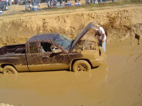 1979 Ford Bronco - Pickup truck stuck deep in a mud pit during an event, with a person inspecting the engine.