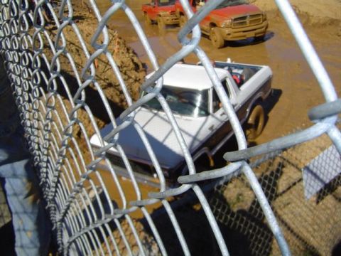 1979 Ford Bronco - A white and brown pickup truck navigates a muddy track, with another vehicle visible in the background.