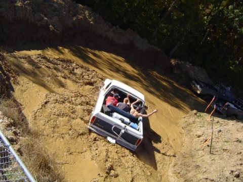 1979 Ford Bronco - A white 1979 Ford Bronco navigates a muddy incline, with several passengers riding in the open bed.