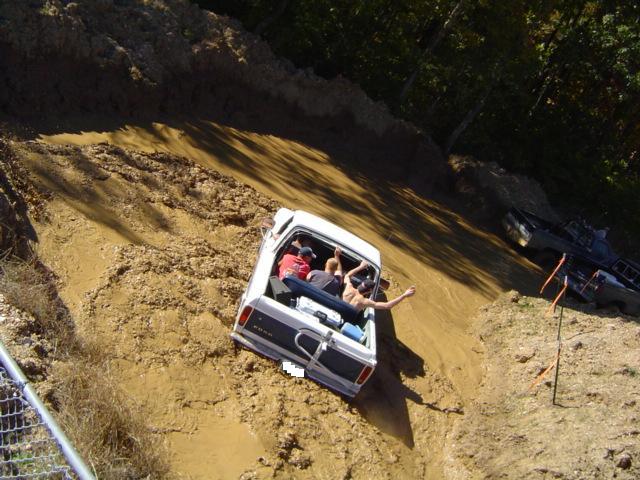 White 1979 Ford Bronco stuck in mud with people in the bed