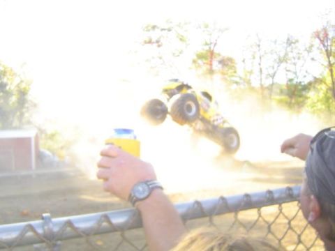 1979 Ford Bronco - A monster truck performs a jump, sending dust flying as a spectator watches.