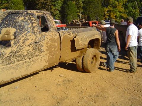 1979 Ford Bronco - A group of people gather around a heavily mud-caked pickup truck during an off-road event.