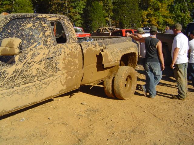 Mud-covered pickup truck with dual rear wheels and people standing nearby