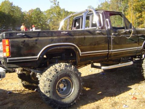 1979 Ford Bronco - Modified black pickup truck with off-road tires and a chrome roll bar, seen from the side.