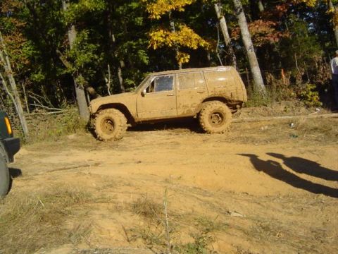 1979 Ford Bronco - An SUV covered in mud navigates a dirt track during an off-road event.