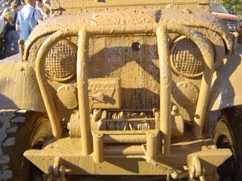 1979 Ford Bronco - A heavily mud-covered vehicle's front end is visible, with people in the background.