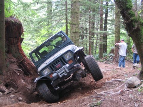 1990 Ford Bronco - A Jeep Wrangler navigates a steep, wooded trail, tilting precariously as it goes.