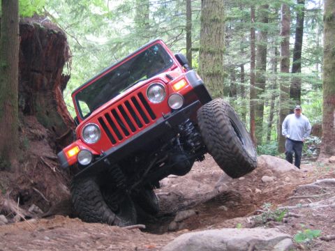 1990 Ford Bronco - A red Jeep Wrangler navigates a challenging off-road trail, demonstrating its articulation.