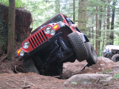 1990 Ford Bronco - A red Jeep Wrangler navigates a challenging off-road course with steep inclines and large rocks, while another vehicle is visible in the di…