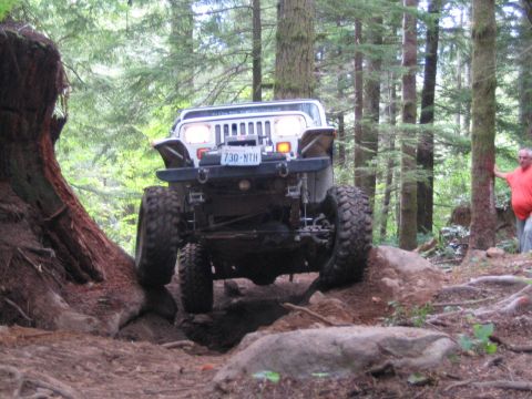 1990 Ford Bronco - Jeep Wrangler navigates a challenging rocky path through a dense forest.