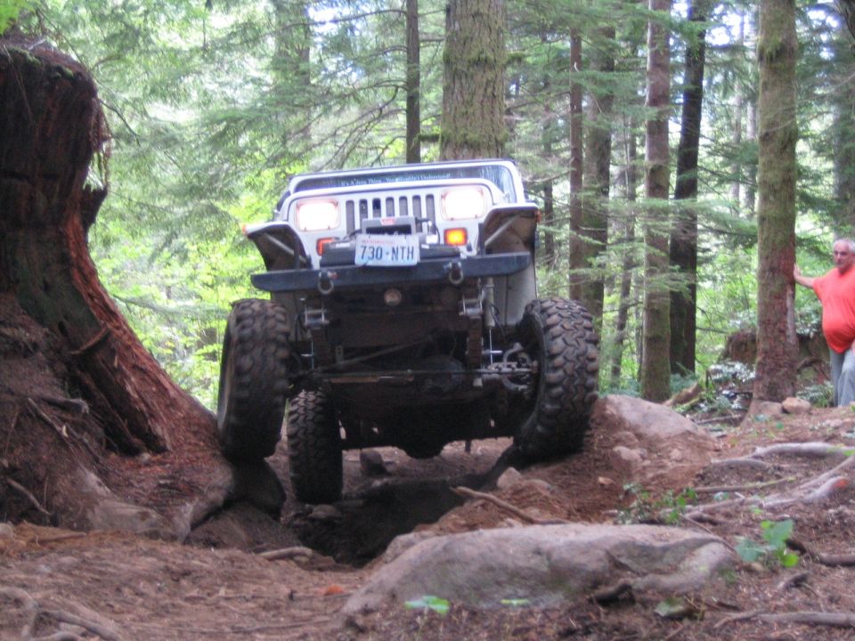 Jeep Wrangler climbing over rocks on a forest trail, license plate 730-NTH