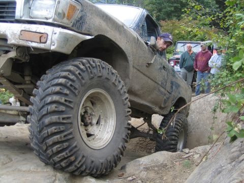 1990 Ford Bronco - This heavily modified truck is shown off-roading with other vehicles in the background.
