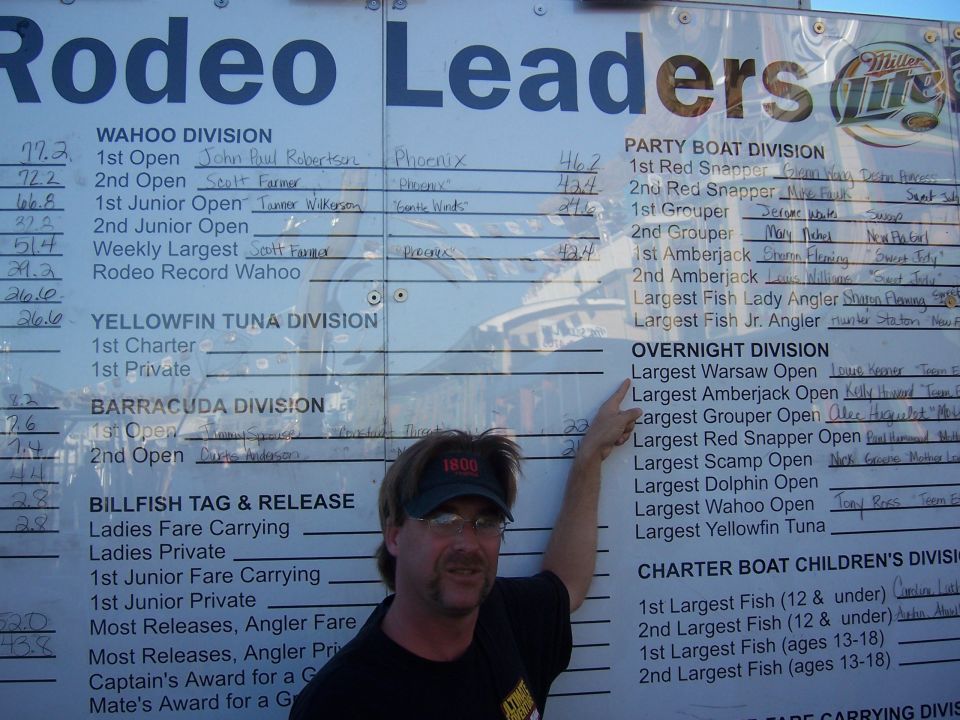 Man pointing at a large scoreboard listing fishing tournament results