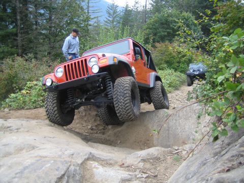 1990 Ford Bronco - Two Jeeps navigate a challenging rocky off-road trail surrounded by trees and hills.