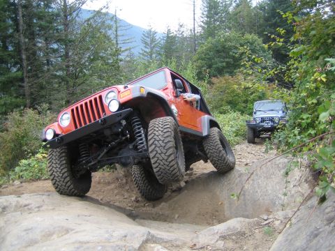 1990 Ford Bronco - Two Jeeps tackle a challenging off-road course on a wooded mountain trail.