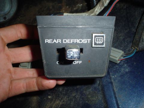 1984 Ford Bronco - A hand holds a rear defrost switch from a vehicle's interior.