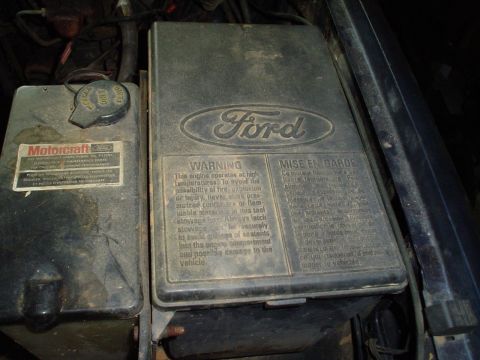 1984 Ford Bronco - Close-up of engine compartment components, including a Motorcraft cap and a Ford warning label.