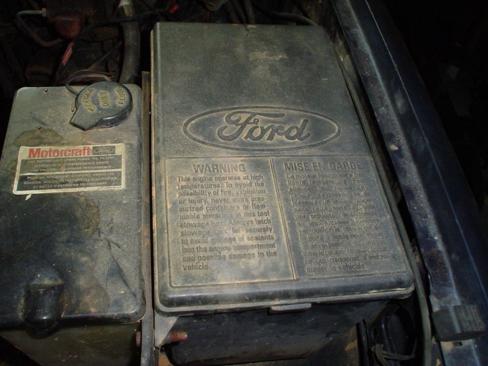 Ford engine compartment with Motorcraft fluid cap and warning label on a black box