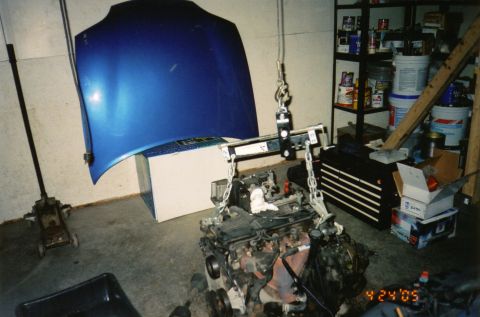 1996 Chevrolet Cavalier - Engine removal in progress, with the hood propped open and supported by a hoist.