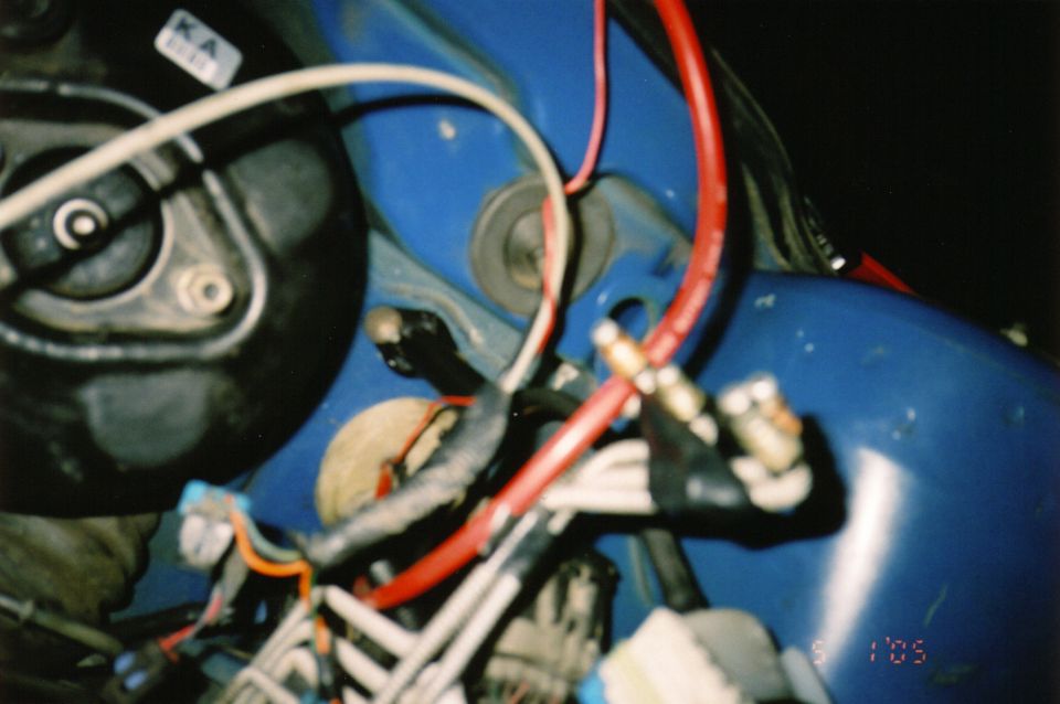 Close-up of messy wiring harness in a blue engine bay, with red and white wires prominent