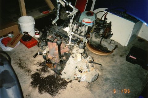 1996 Chevrolet Cavalier - A disassembled engine and transmission unit rests on a concrete floor, surrounded by tools and debris.