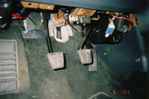 1996 Chevrolet Cavalier - Driver's footwell of a car with the lower dash trim removed, showing the clutch and brake pedals on gray carpet plus the exposed pedal-box…