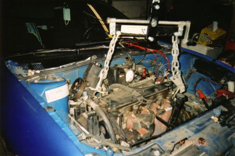 1996 Chevrolet Cavalier - Engine bay of a blue car during an engine pull, with a load leveler bar and chains hooked to the cylinder head and the hoist above. The eng…