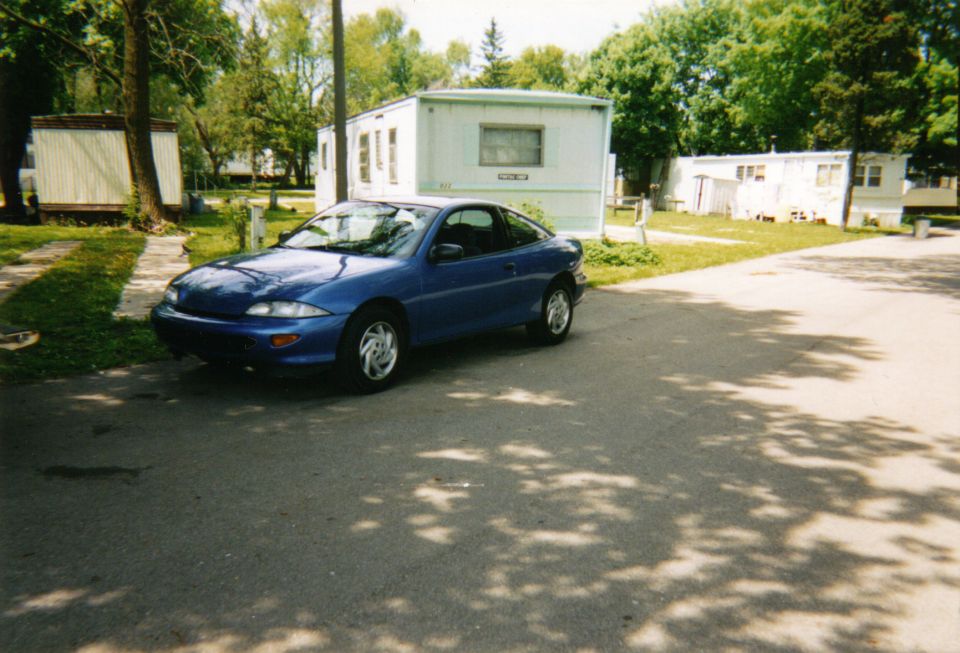 blue coupe parked in front of trailer homes