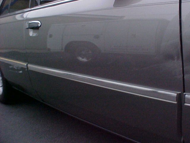 Reflection of a white work van on the side of a dark car