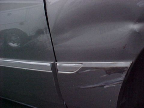 2000 Mercury Grand Marquis - Gray sedan shows damage to the fender and door, with chrome trim visible along the lower body.