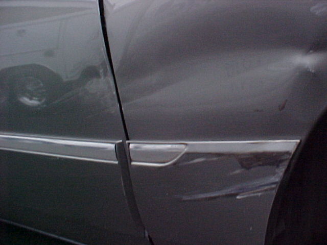 Gray sedan door and fender with chrome trim, showing damage and scratches