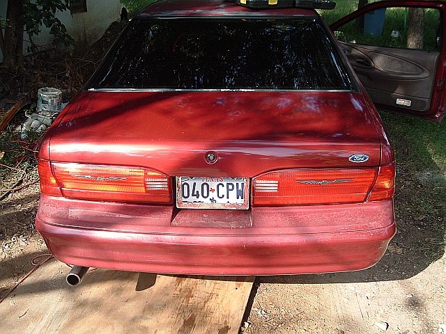 Rear of a dark red Ford with Texas plate 040 CPW, driver door open, parked on dirt