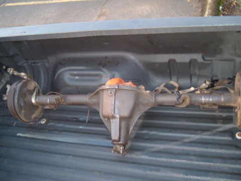 1989 Ford Bronco - A rear axle assembly, likely from a truck or SUV, is secured with straps inside a pickup truck bed.