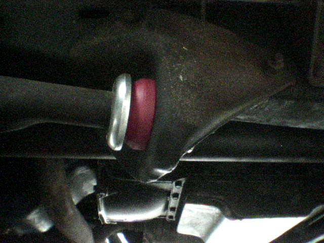 Underside view of a vehicle joint with red bushing and silver collar on a dark metal housing