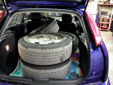 2003 Ford Escape - Open hatchback of a purple/blue compact car loaded with four mounted tires, one on a five-spoke alloy wheel, stacked on a towel over the fo…