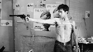 1995 Ford Bronco - A man aims a handgun in a room adorned with posters, his torso bare and jeans on.
