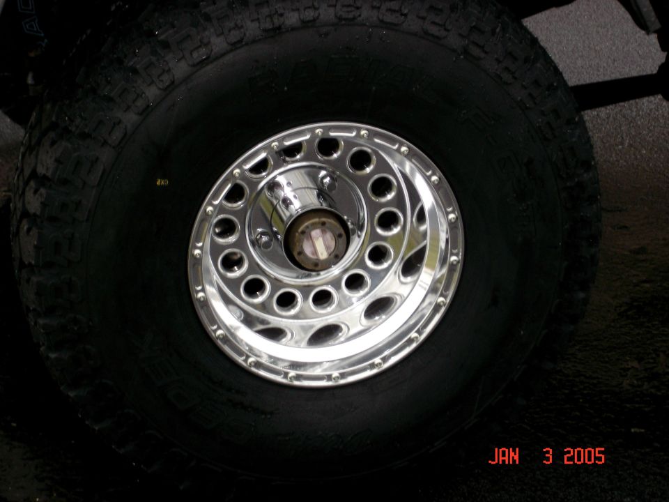 Polished aluminum wheel with round cutouts and exposed chrome hub on an all-terrain tire
