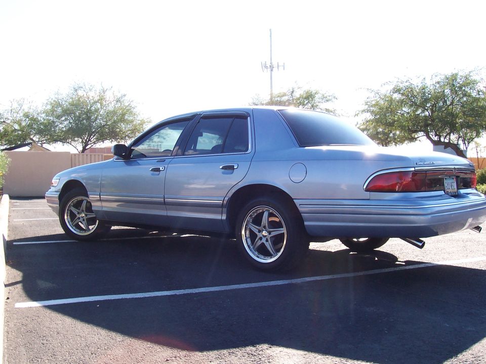 Light blue Mercury Grand Marquis sedan, rear three-quarter view, aftermarket wheels, parked in a lot