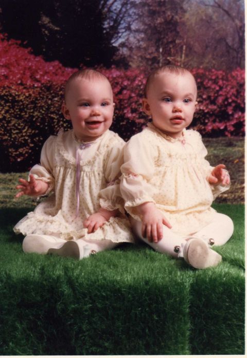 2001 Ford Taurus - Two babies in matching yellow dresses sit on artificial grass, with a backdrop of pink flowers and trees.