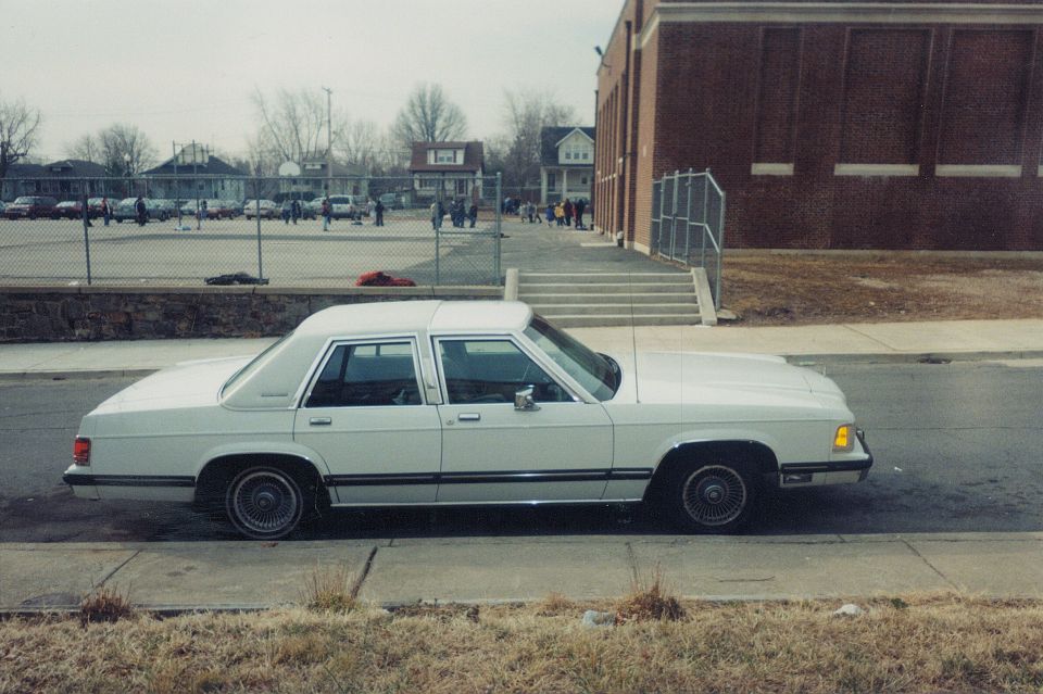 1991 Mercury Grand Marquis parked curbside, side view. Building and schoolyard in background