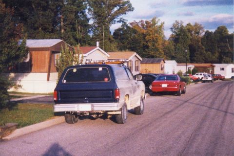 1990 Dodge Charger - A Dodge Ramcharger is parked on a street in front of several mobile homes, with other cars nearby.