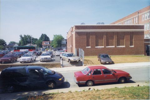 1998 Ford Crown Victoria - A parking lot scene shows multiple vehicles parked near a brick building under a clear sky.