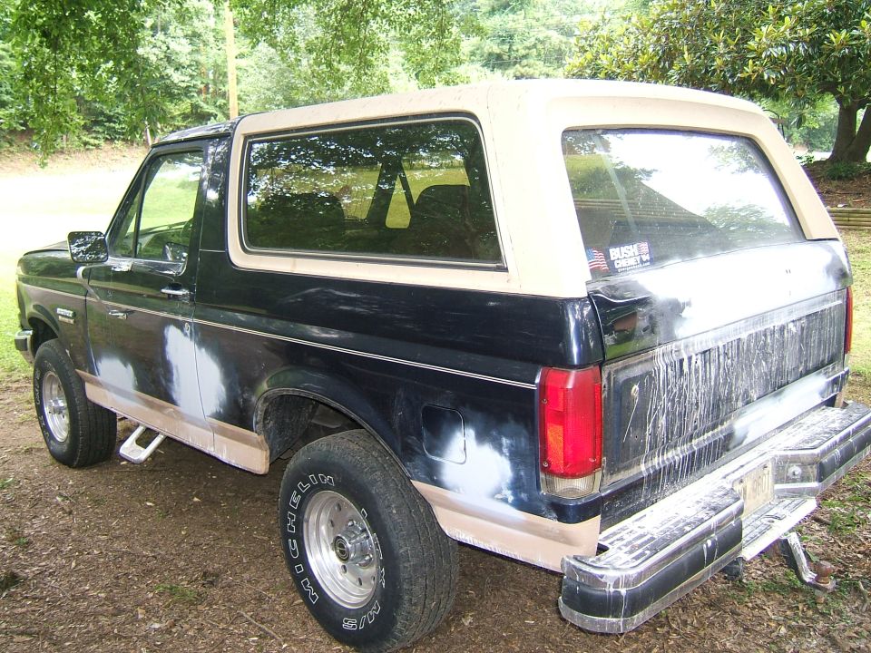 Black and tan Ford Bronco with body filler on the lower panels, viewed from the rear three-quarter angle